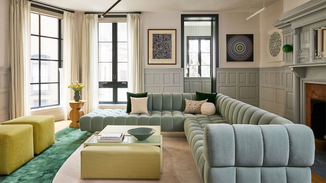 living room with white walls, light blue wainscoting, light blue sofa, yellow coffee table ottoman and stools, green carpet, and windows with curtains