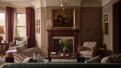 Living room with green velvet sofa, patterned armchairs, pink curtains, marble fireplace, antique artwork and layered lighting.