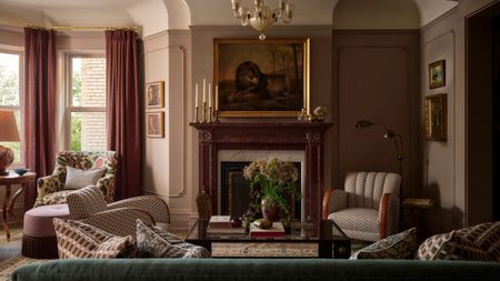 Living room with green velvet sofa, patterned armchairs, pink curtains, marble fireplace, antique artwork and layered lighting.