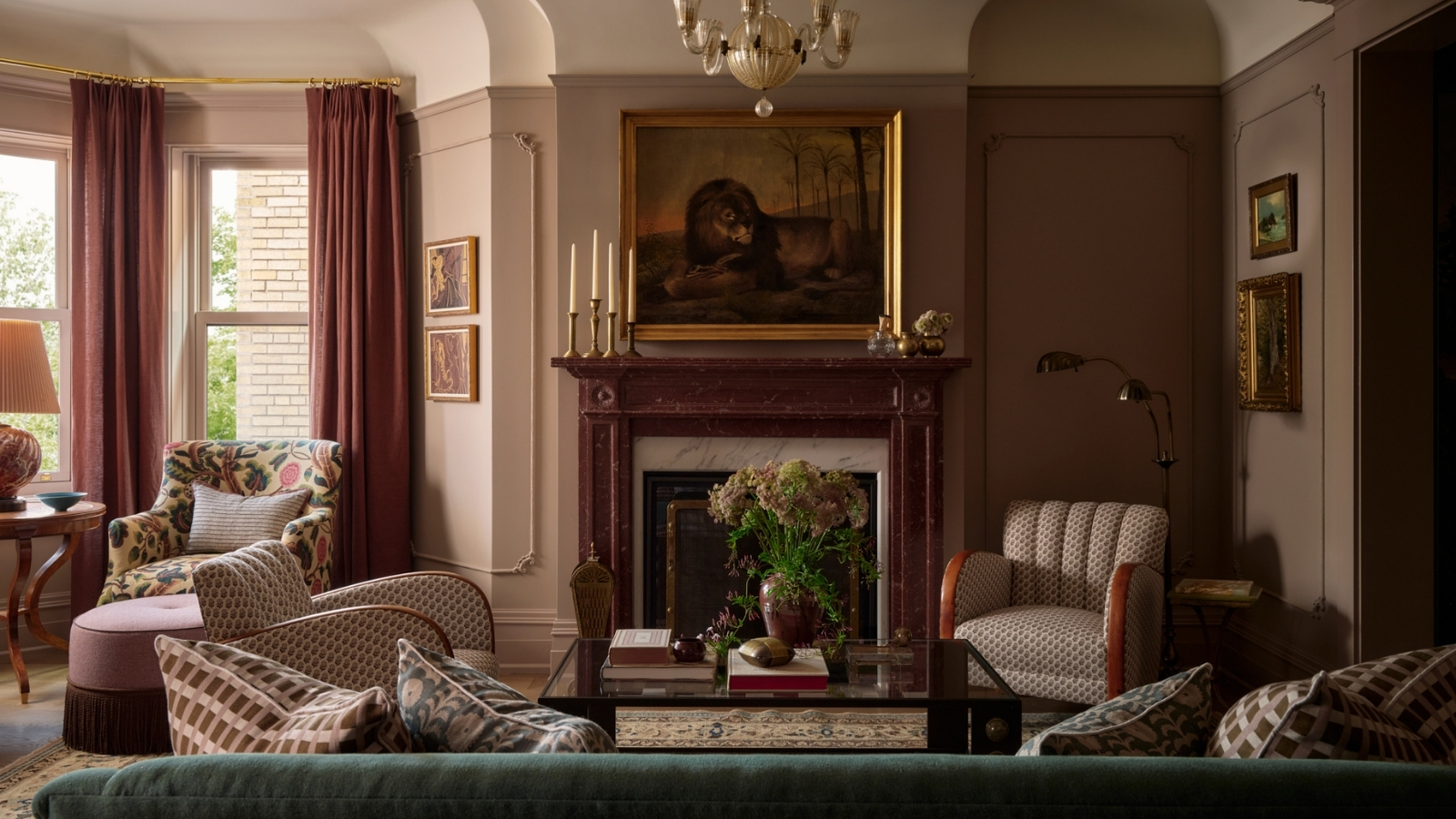 Living room with green velvet sofa, patterned armchairs, pink curtains, marble fireplace, antique artwork and layered lighting.