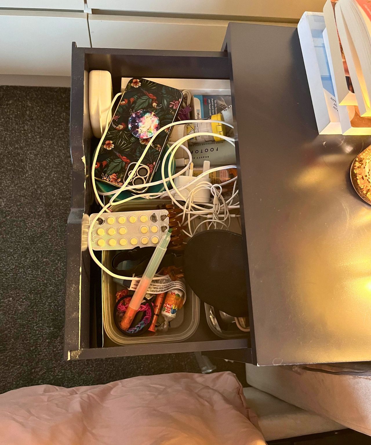 Bedside drawer before open and messy with wires phones and odd bits