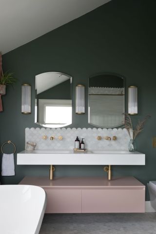 Scallop-shaped tiles form a pretty backdrop for brushed brass tap fittings in a green and pink bathroom