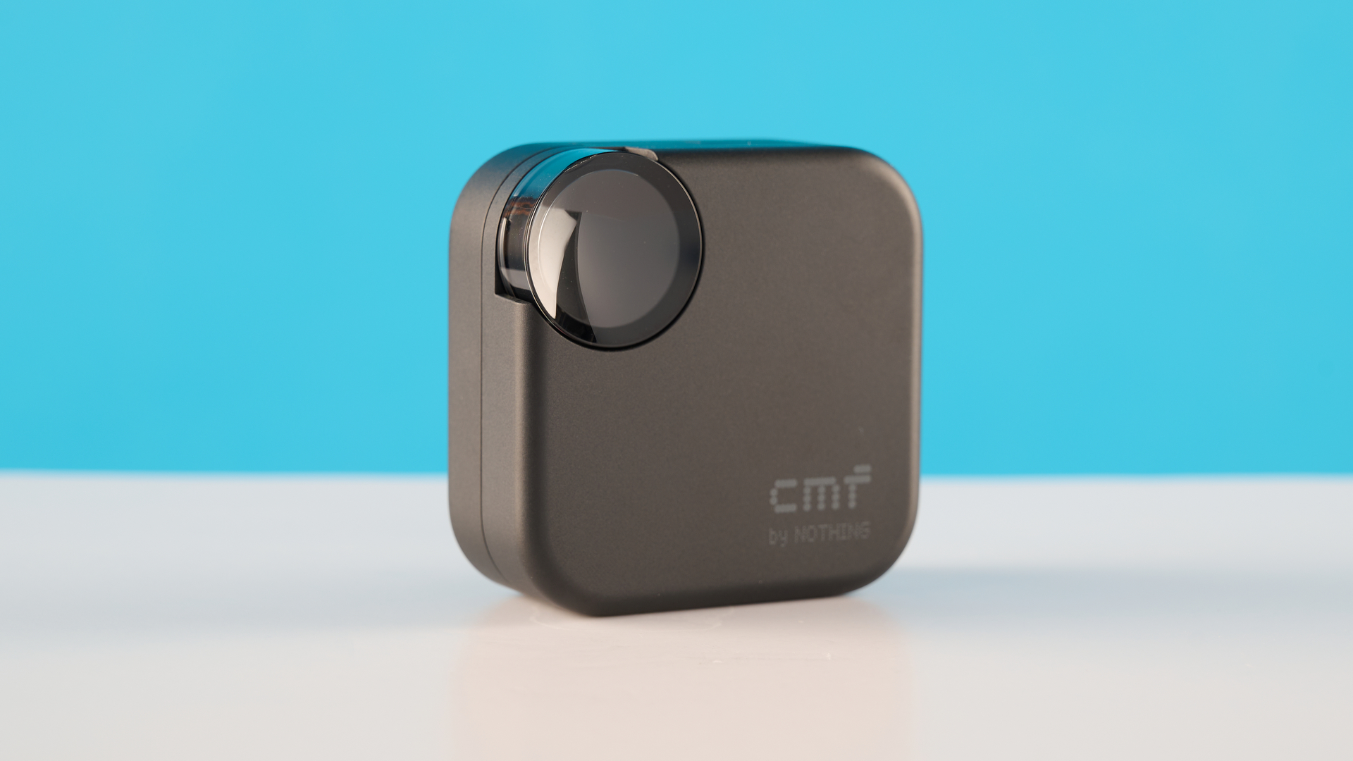 CMF Buds 2 in Dark Gray photographones on a gray table in front of a blue background