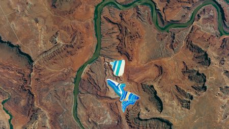 An astronaut photo showing two stripy blue structures next to a green river in the rusty brown landscape of the Colorado Plateau