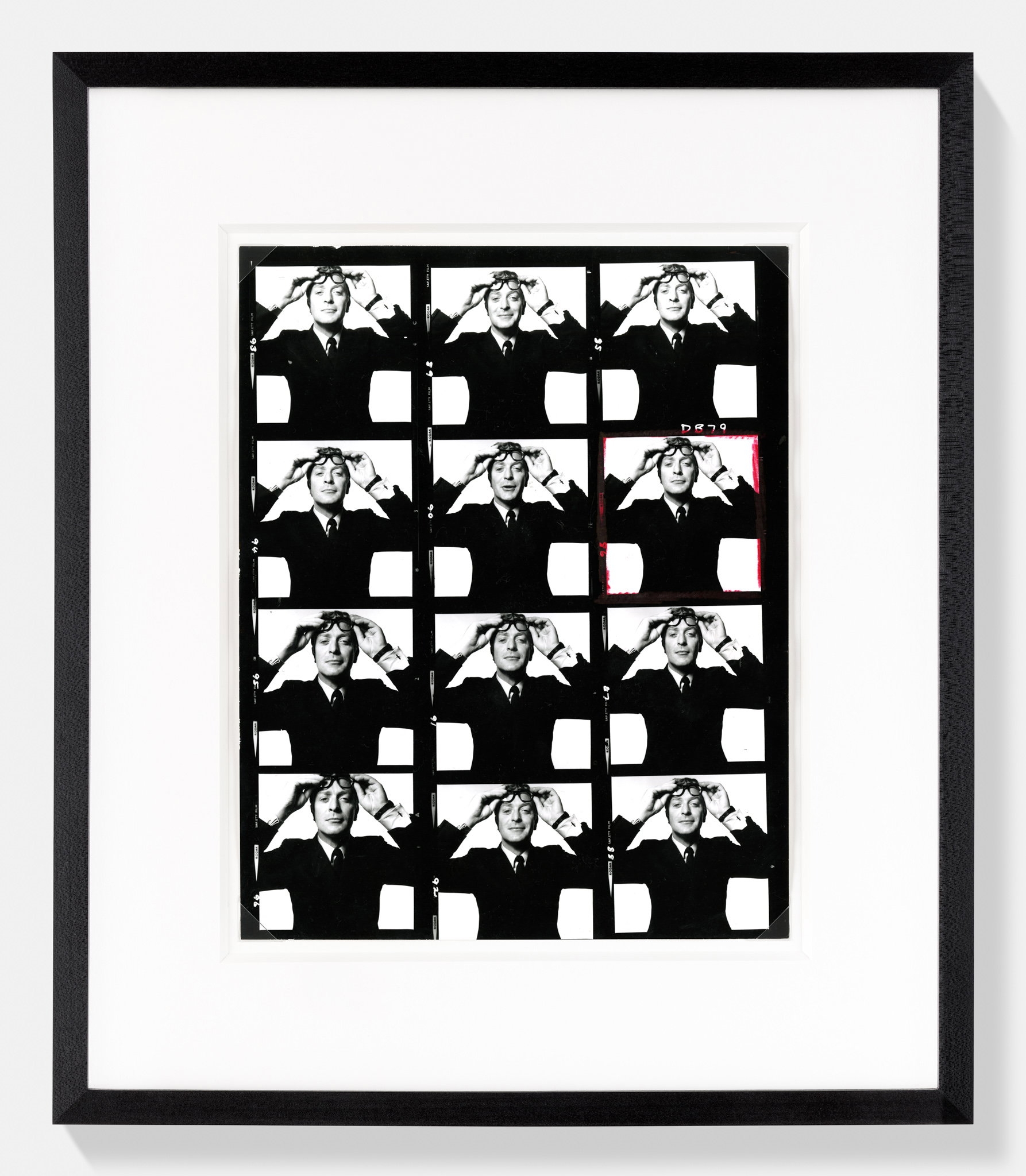 A framed contact sheet of twelve nearly identical Michael Caine portraits, his hand raised to push up his glasses in each repeated frame.