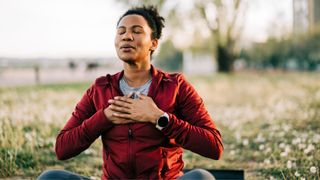 Woman sitting outdoors on grass with hands clasped over chest, practising yoga