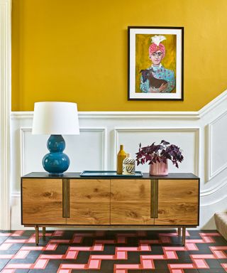 Yellow entryway with colorful floor, white wall panels and wood console