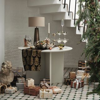 A Christmas decorated staircase with a table underneath adorned with decorations and products from the Wisdom & Wonder range by John Lewis