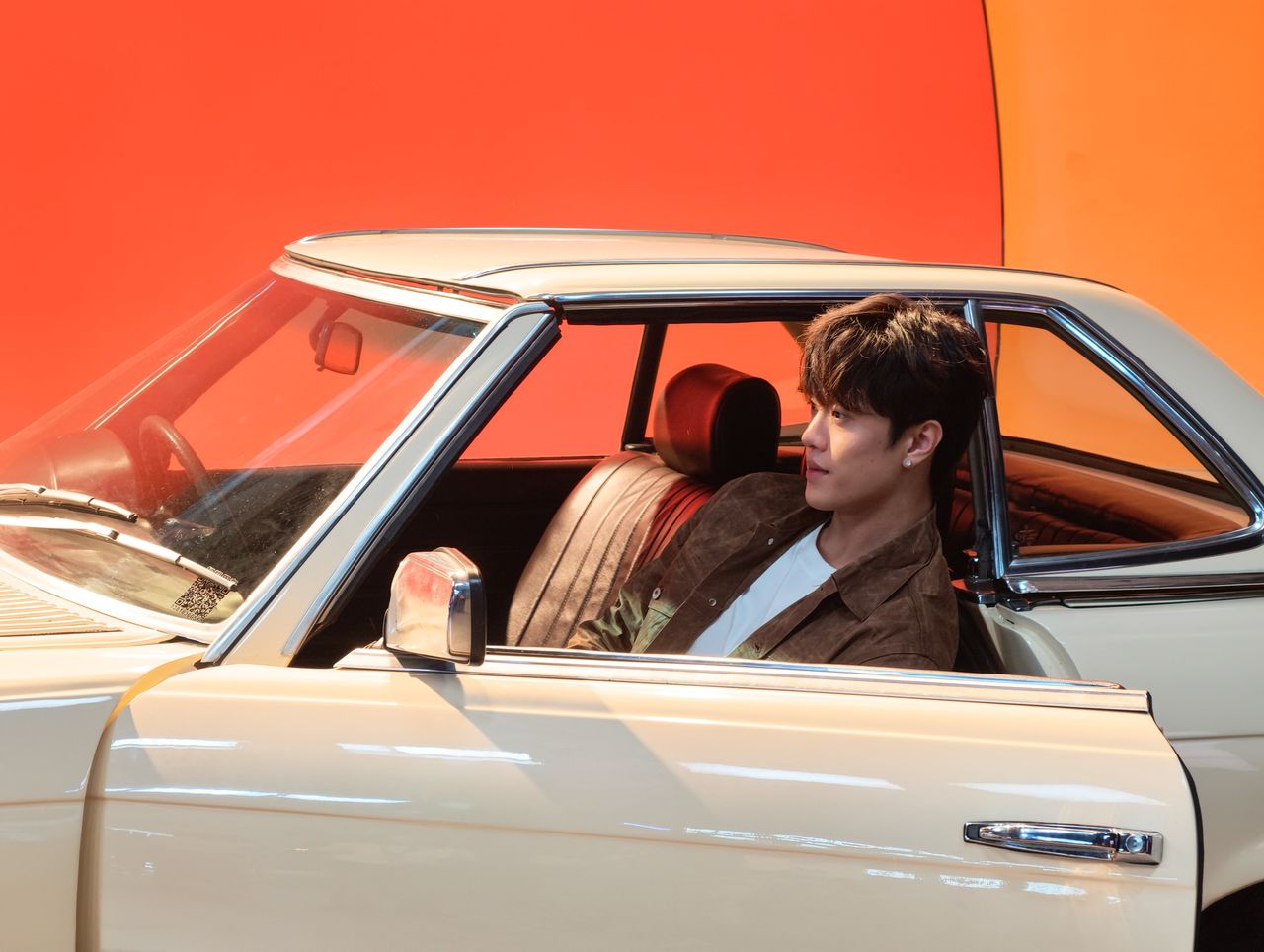 Man in a classic Mercedes with the driver's door open &mdash; there's a bright red and orange studio backdrop