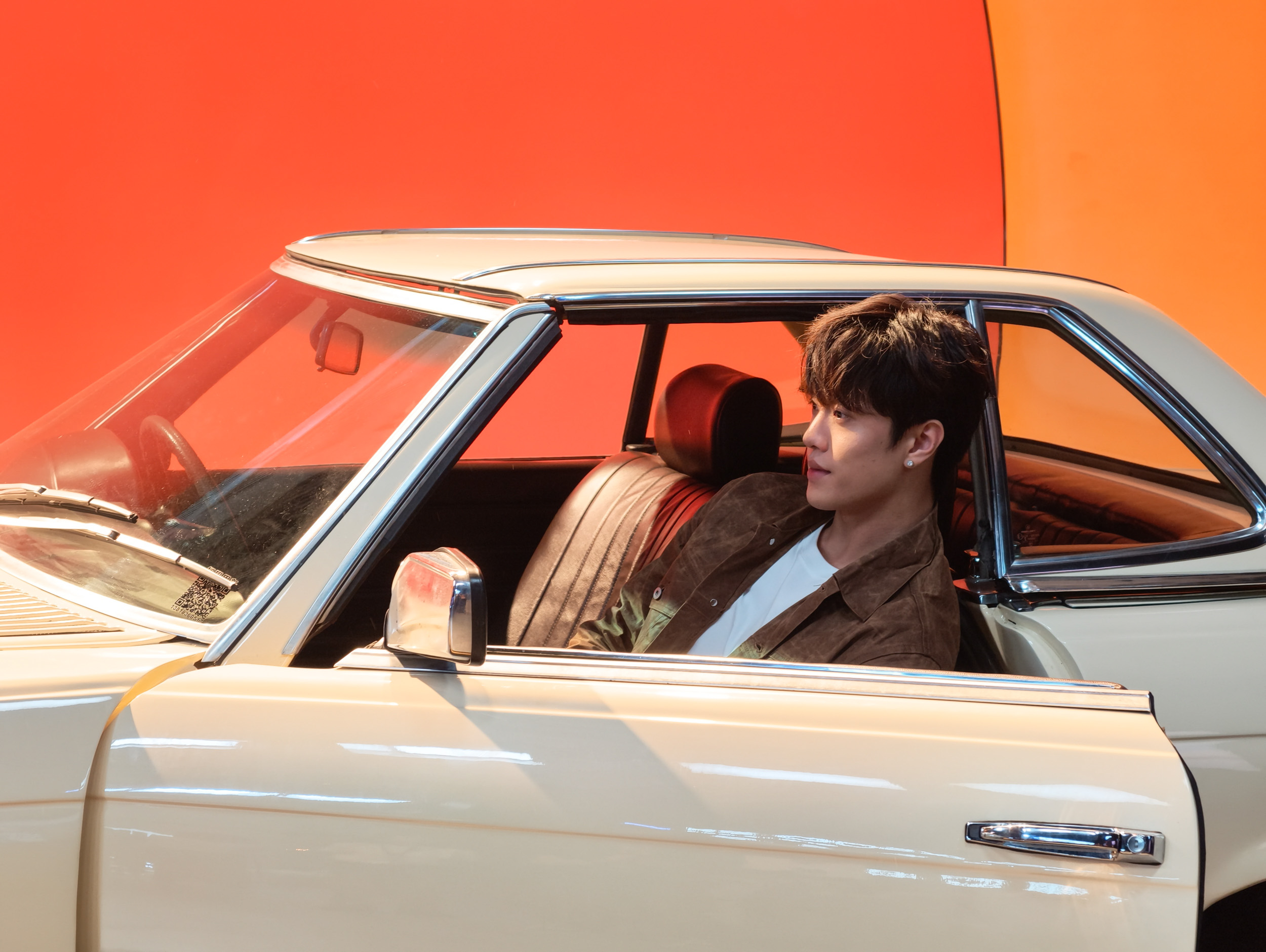 Man in a classic Mercedes with the driver's door open — there's a bright red and orange studio backdrop