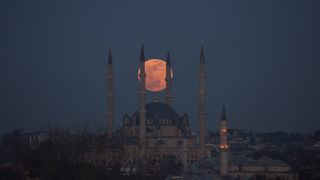 full moon shining a pinky orange hue being a mosque.