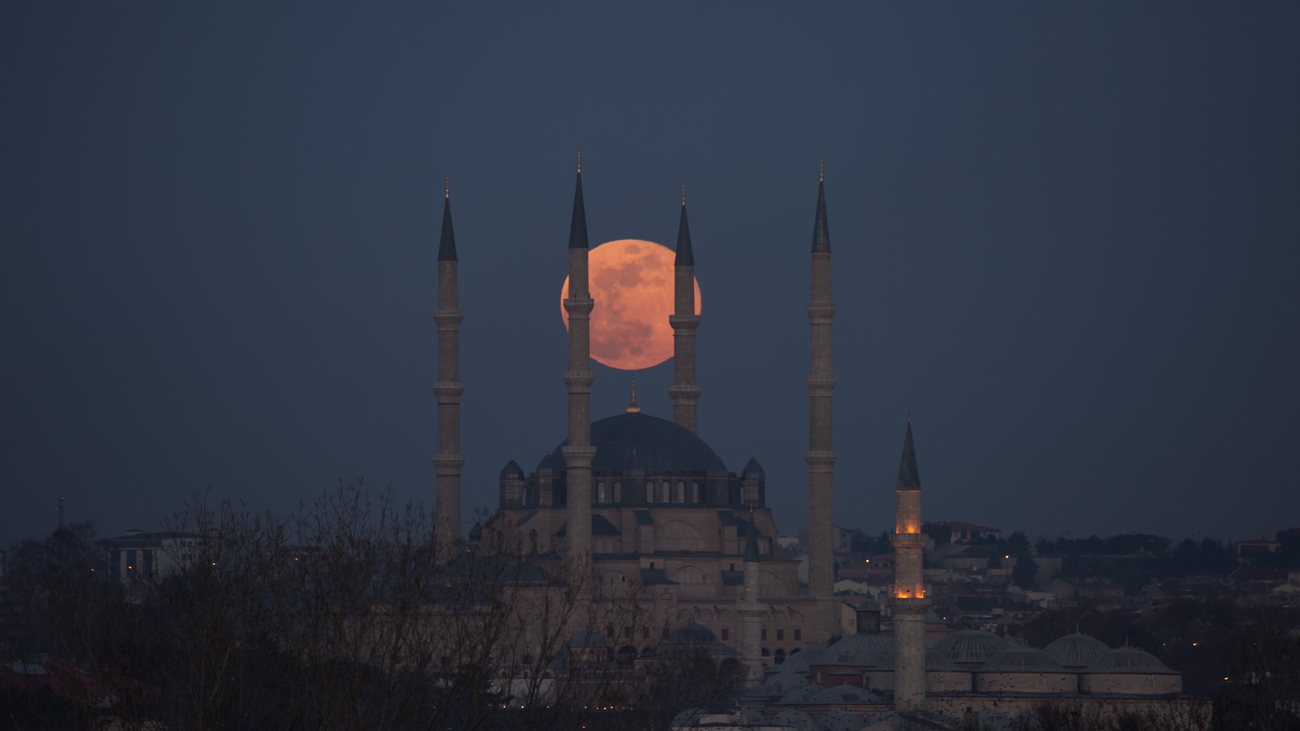 full moon shining a pinky orange hue being a mosque.