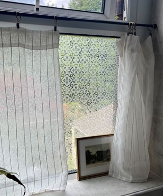 A tension rod being used to hang half curtains in front of a patterned window.