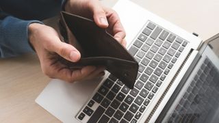 Man holding an empty wallet with laptop in background