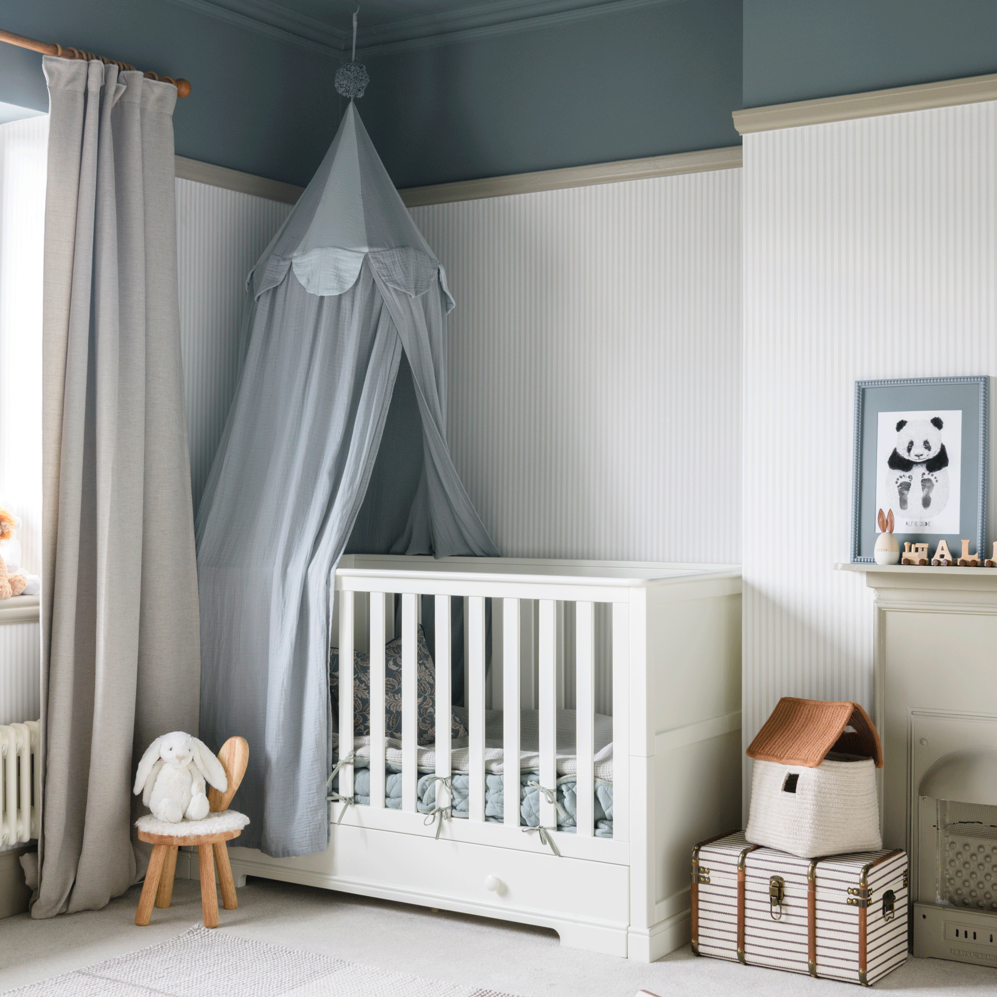 a child's bedroom with a cot, blue canopy and wallpapered walls with blue painted area above the picture rail