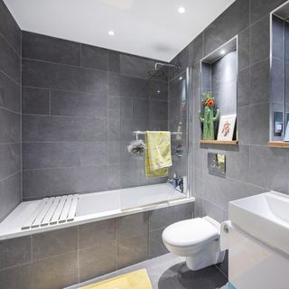 Grey tiled bathroom with combined shower and bath and alcove storage shelves