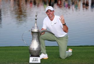 Rory McIlroy holds up four fingers whilst standing next to the Dubai Desert Classic trophy