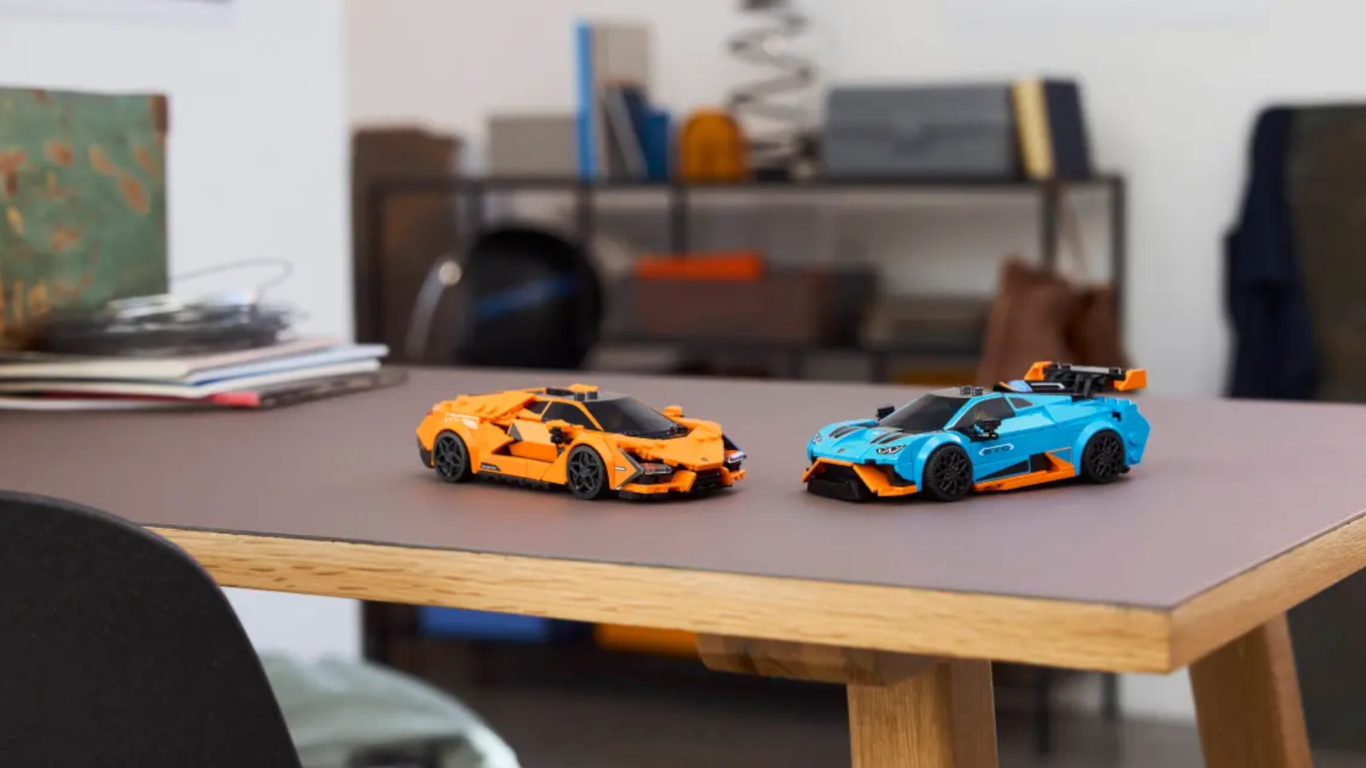 Two Lego cars on a dark-topped table, facing one another, with shelves in the background