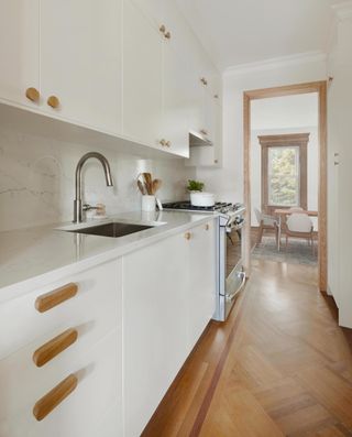 Galley kitchen with white cabinets and wood hardware