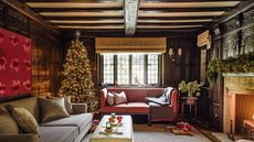 A cozy living room with two sofas, with exposed ceiling beams, a tall decorated Christmas tree and fireplace with a lit fire.