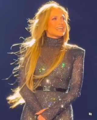 A photo of Jennifer Lopez beaming in a chrome onesie accessorized with a black belt and ankle boots at Saadiyat Nights.