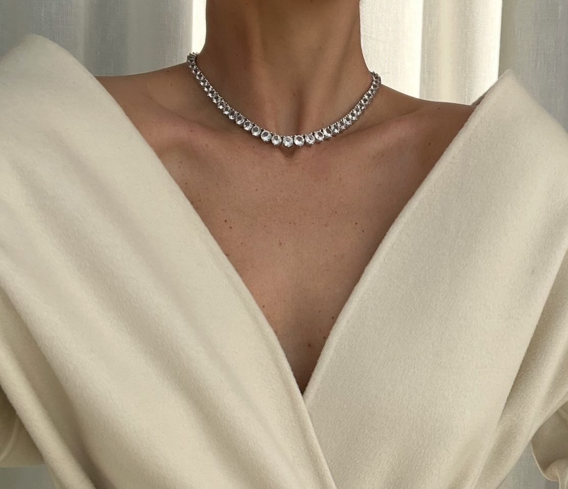 A close-up of @rikkekrefting wearing a v-neck cream top and a diamond tennis necklace