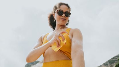 Woman putting on suncream wearing a bikini on the beach, representing how to heal sunburn faster