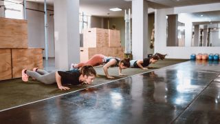 Three women perform chest-to-floor burpees in a line