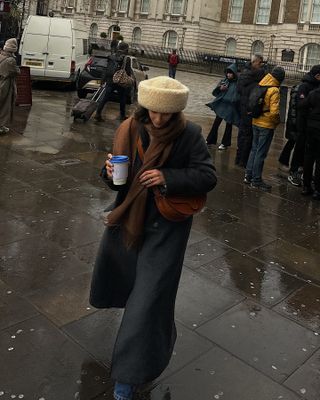 Fashion influencer @_santinaharrison wears a chic and practical look with a shearling hat and long coat that's on-trend for 2025.