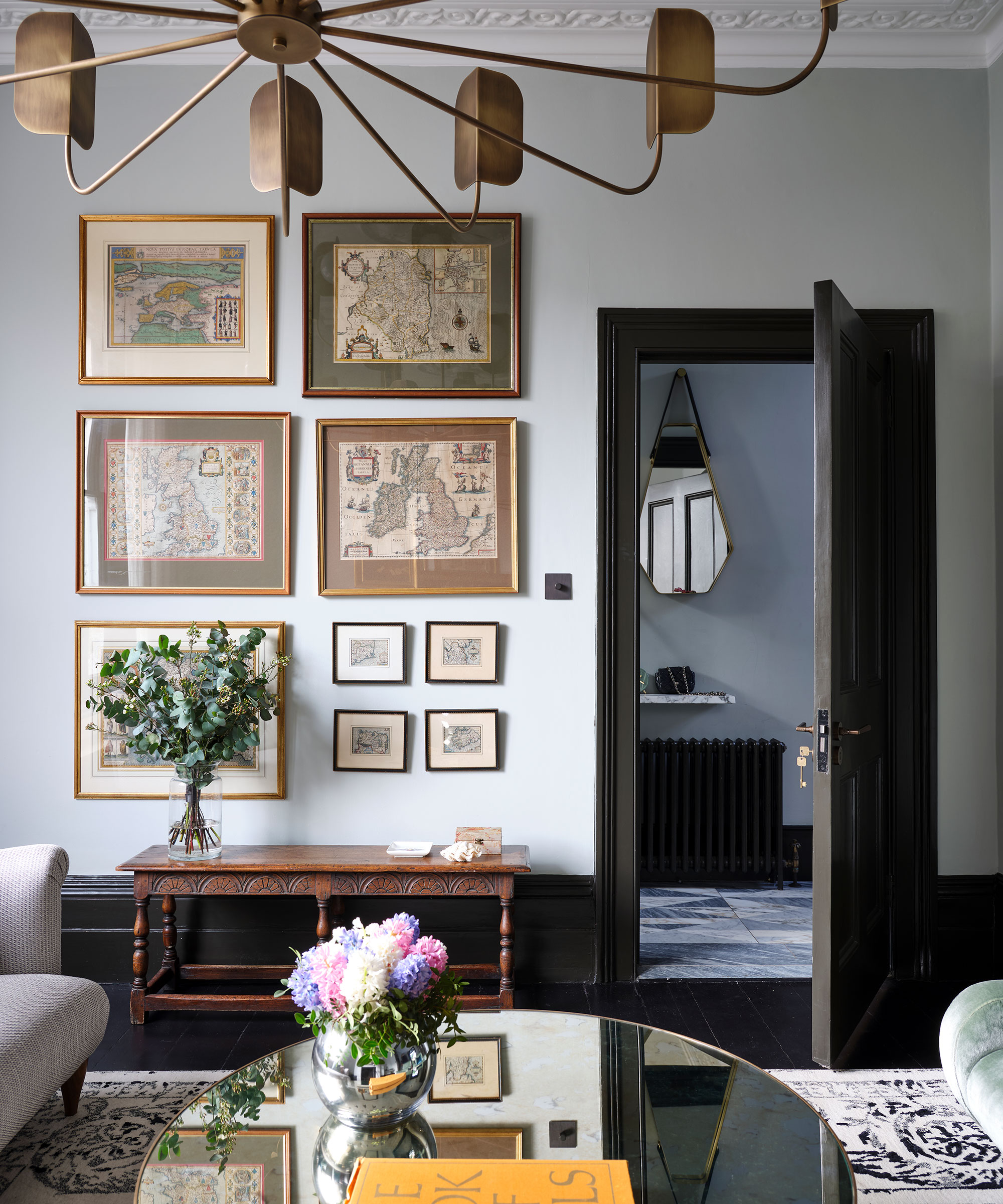 A white-gray neutral living room iwth gallery wall, antique side table and statement gold ceiling light.
