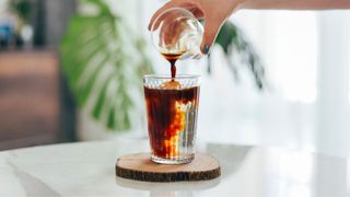 An glass of water with an espresso being poured in on a wooden coaster