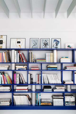 Dark blue bookshelf with many books and framed pictures