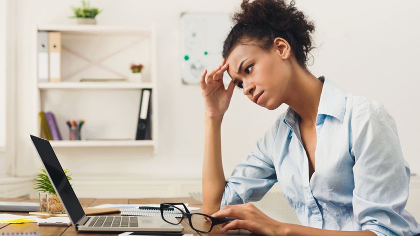 A sad woman looks at her MacBook while rubbing her temples in frustration