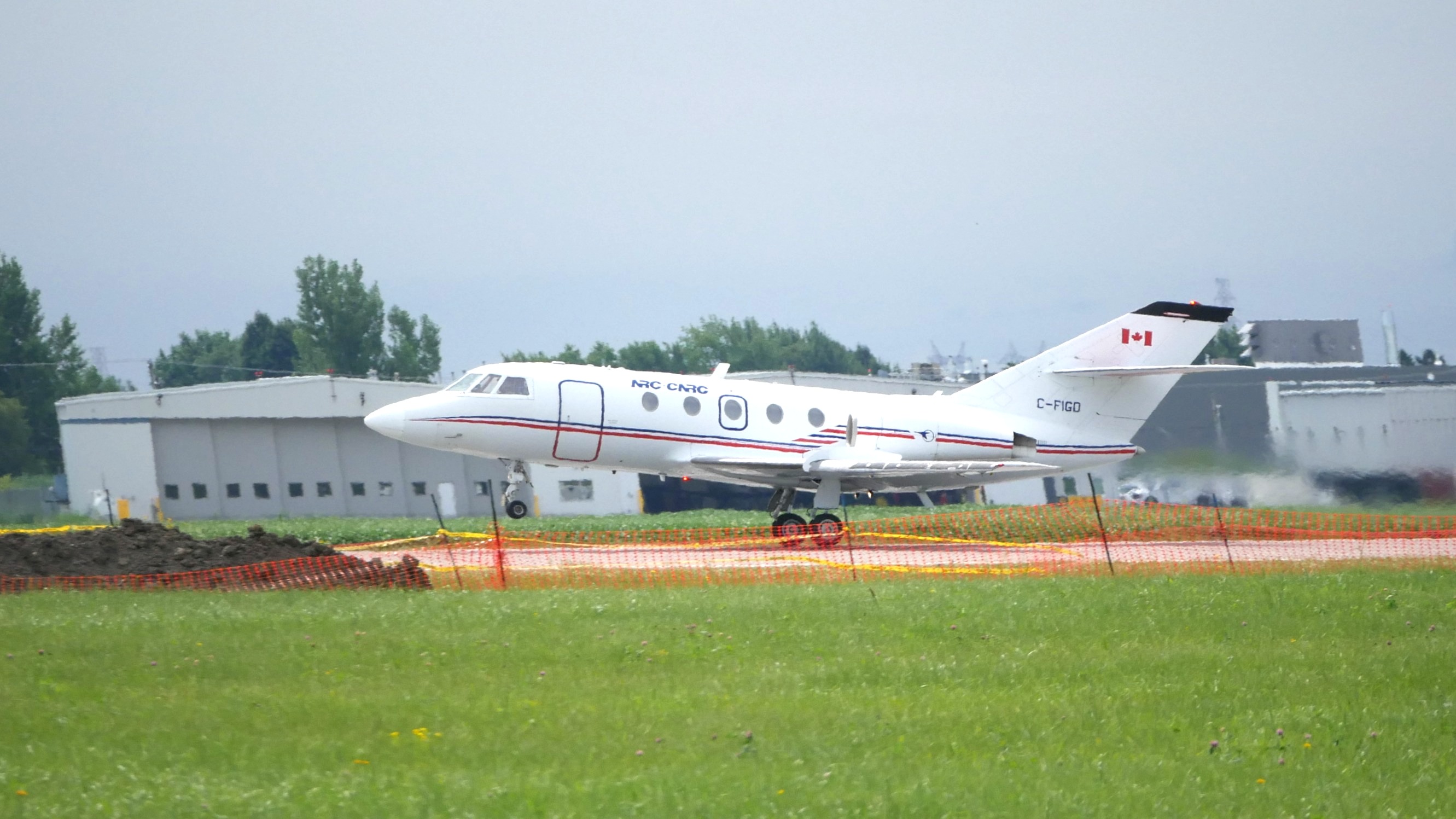 long business plane taking off from runway. grass and construction fence in front