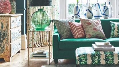 A living room with an emerald green sofa paired with a botanical-print ottoman and matching cushion on the sofa