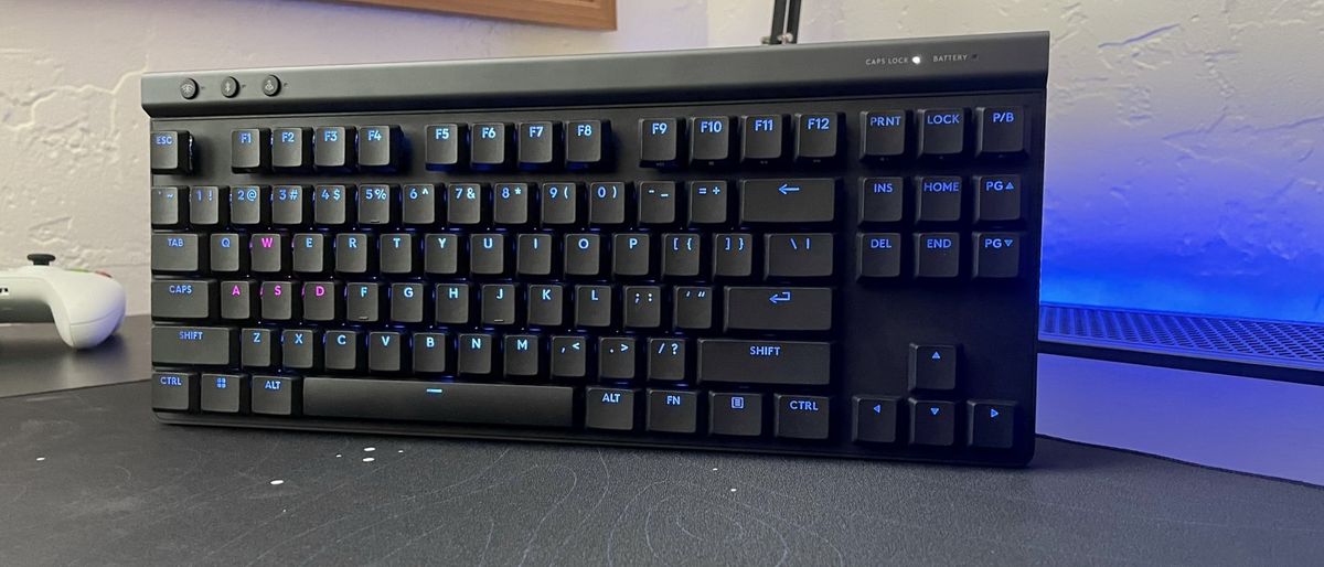 The Logitech G515 LIGHTSPEED TKL gaming keyboard standing on a black desk next to a game controller