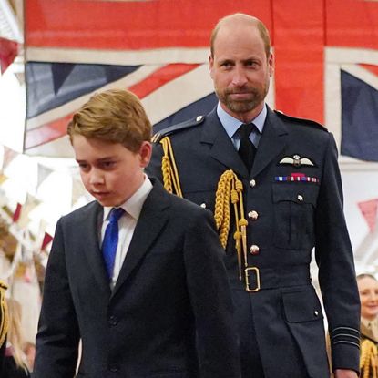 Kate Middleton looks at Prince William, who is wearing military uniform in front of the British flag, while Prince George walks with his head down