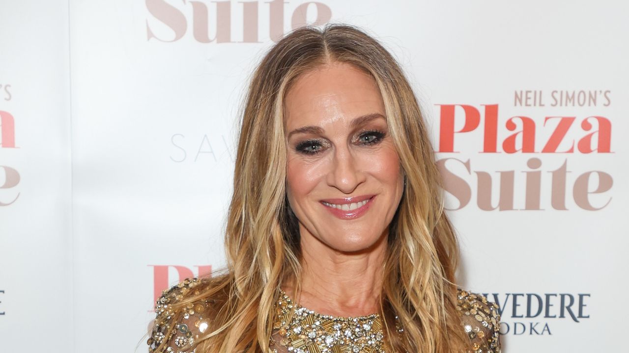 SJP stands in front of a step and repeat with smoky eye makeup