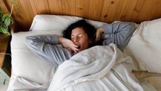 A person lying on their back in bed and yawning
