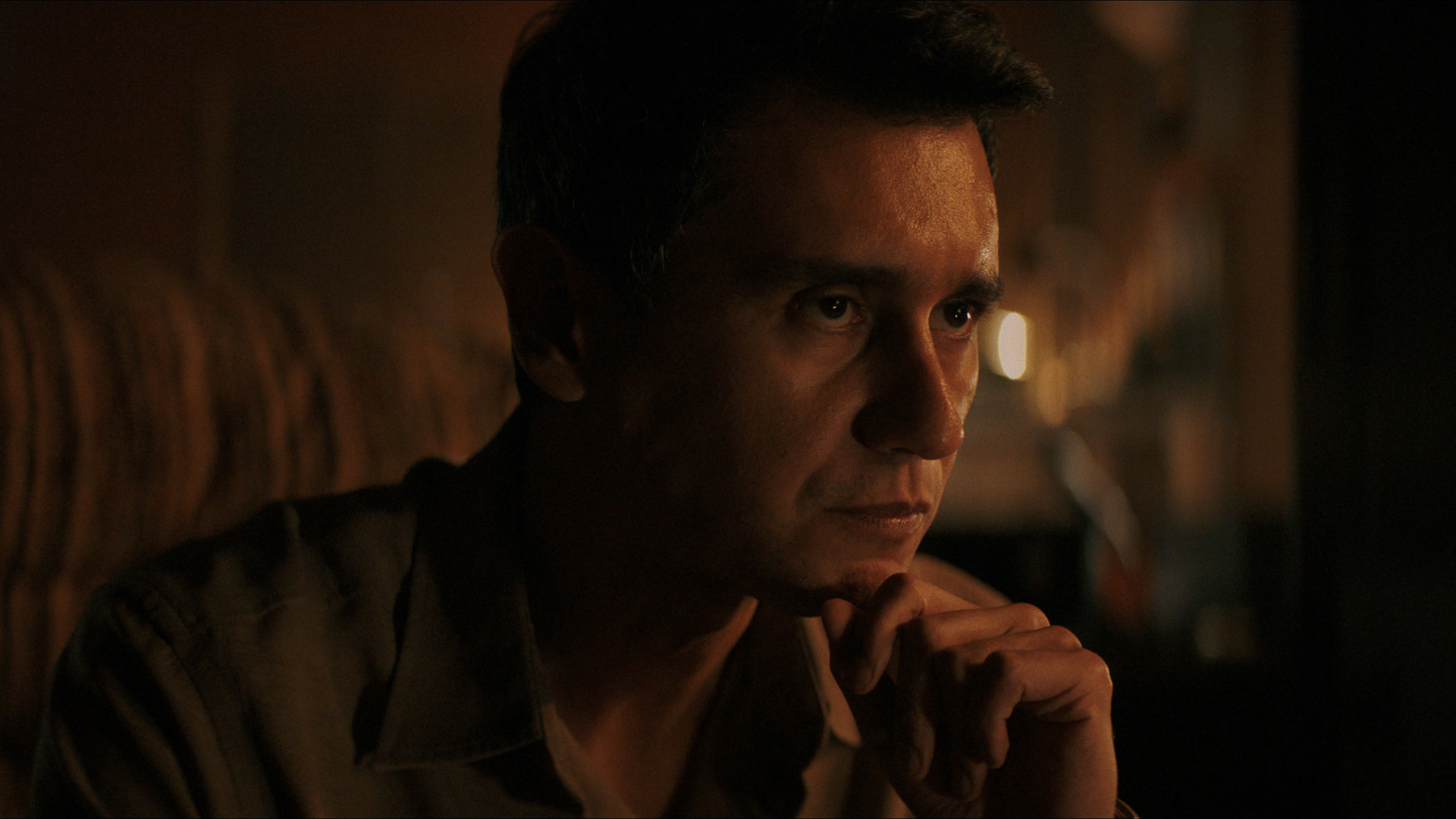 Manusos resting his chin on his left hand in Pluribus episode 4