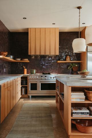 A kitchen with wooden cabinetry and dark brown gloss tiles up the walls