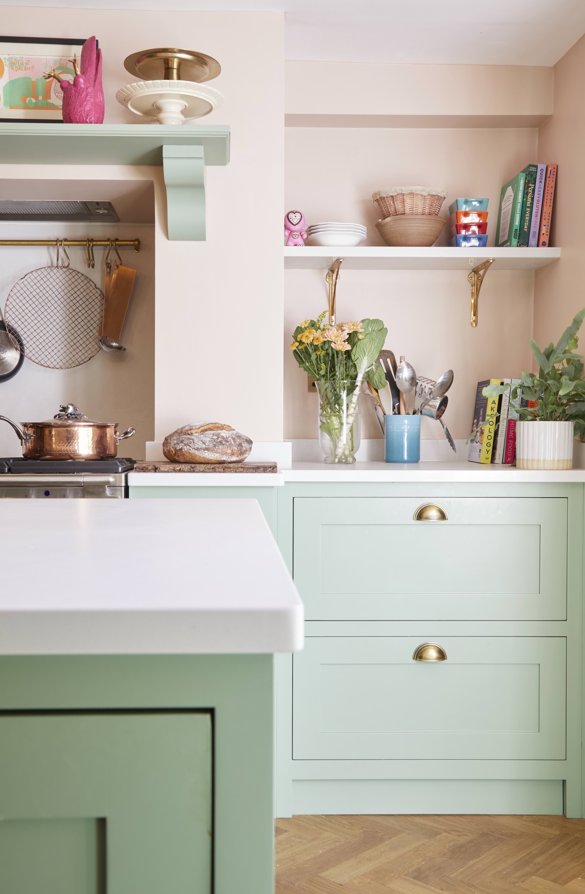 A pink and green kitchen with open shelving in the alcove. On the shelf are books and other kitchen essentials