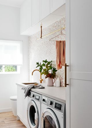 Small laundry room ideas incorporated into a white bathroom with mosaic tiles and gold faucet.