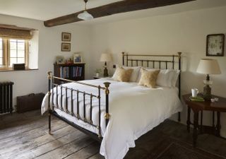 iron bed with white bedlinen and gold pillows in bedroom with cream walls and wooden flooring