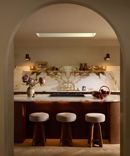 a kitchen seen through an arched doorway with three modern stools in front of a wood island