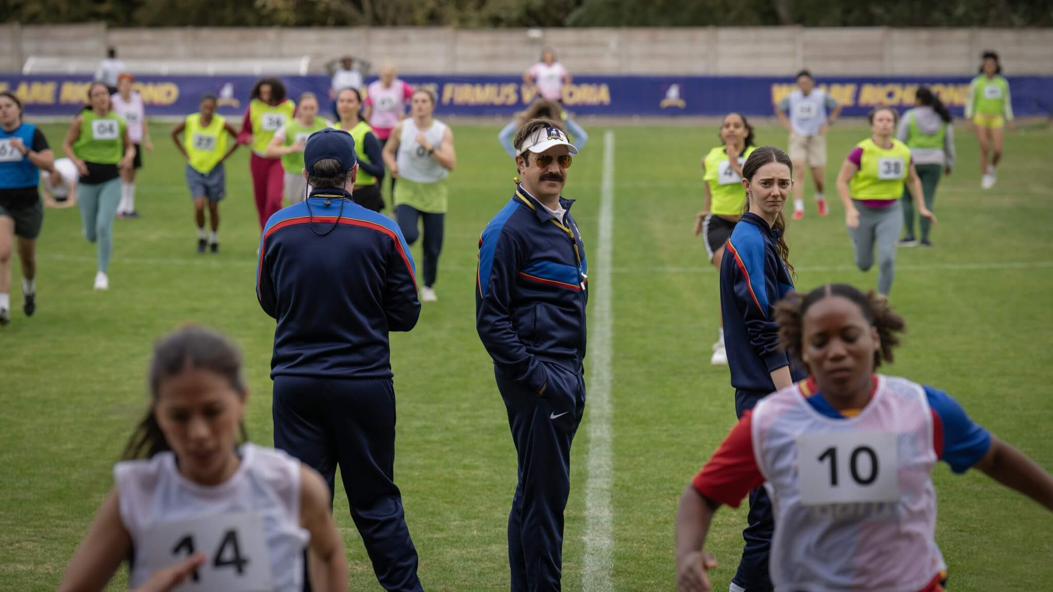 L-R: Brendan Hunt, Jason Sudeikis and Tanya Reynolds on the pitch during training drills in a first-look still from "Ted Lasso" season 4