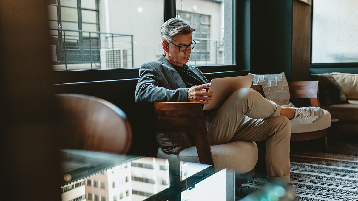 A businessman sitting on a sofa in an office building working on a laptop