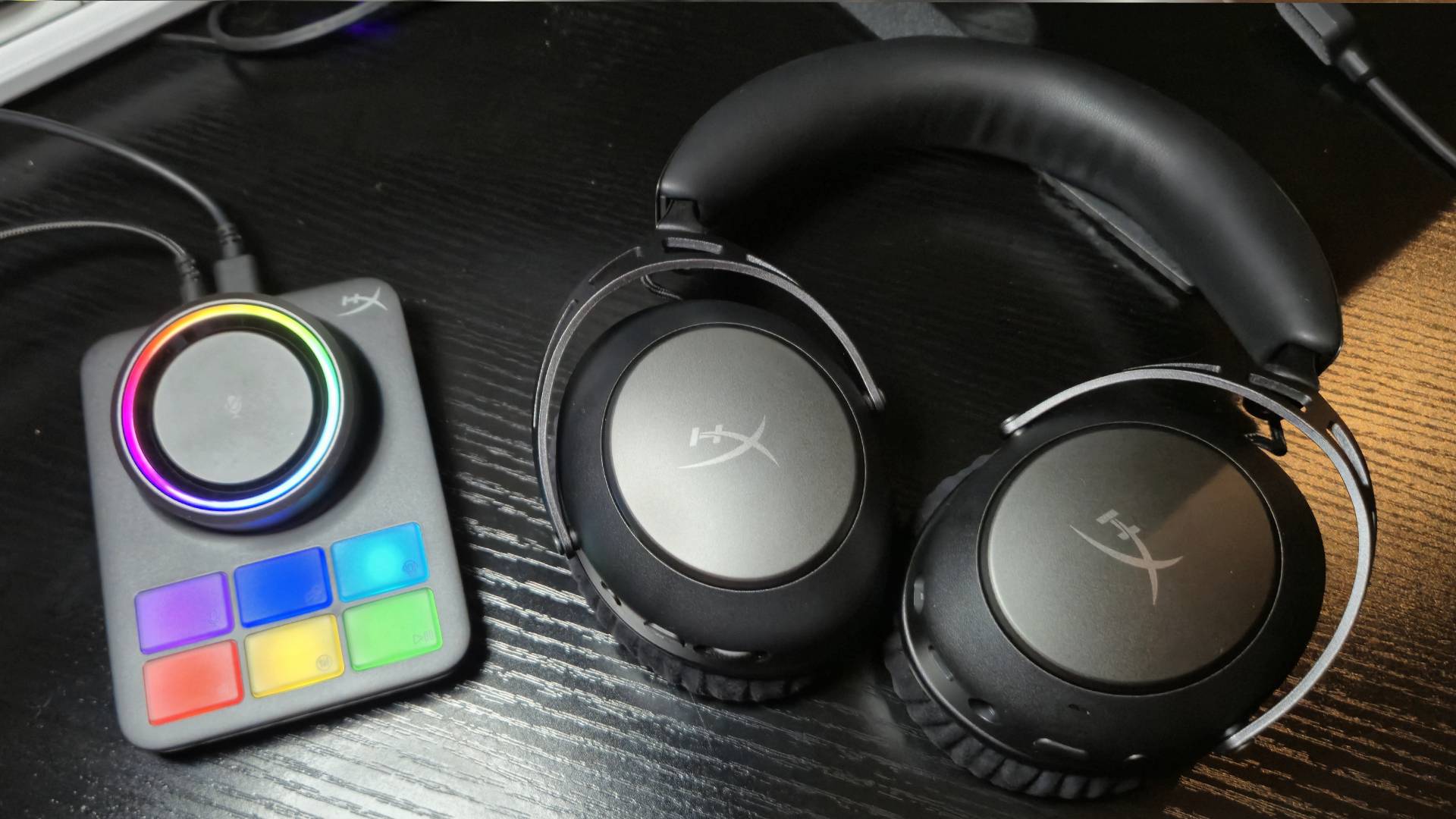 Photo showing a rainbow lit up base station sitting next to a metal black headset on a black desk.