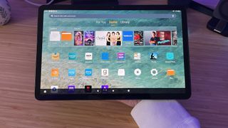 Amazon Fire Max 11 being held along the back panel over a wooden desk