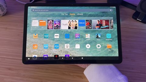 Amazon Fire Max 11 being held along the back panel over a wooden desk
